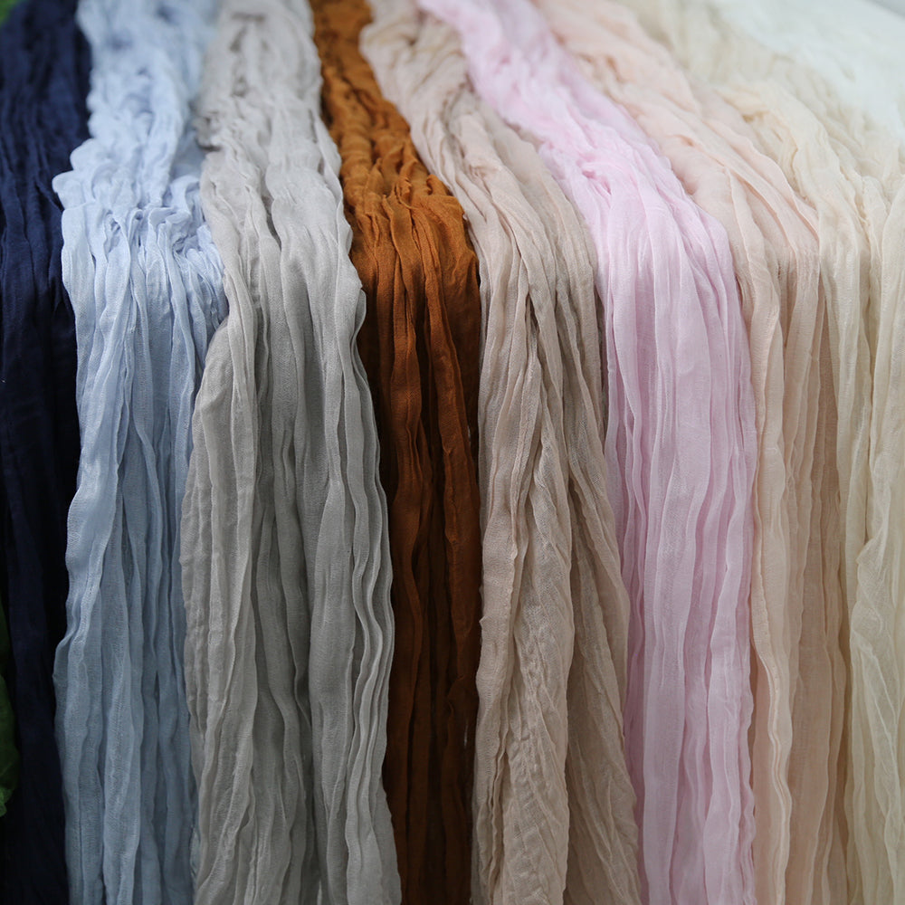 Gauze table runners available in various colors, featuring a soft, textured fabric. The range of colors includes burnt orange, blush pink, dusty blue, dusty pink, ivory cream, light grey, navy, off white, olive green, and sand. Each runner adds a unique and stylish touch to table settings, enhancing the overall ambiance with their elegant and versatile design.