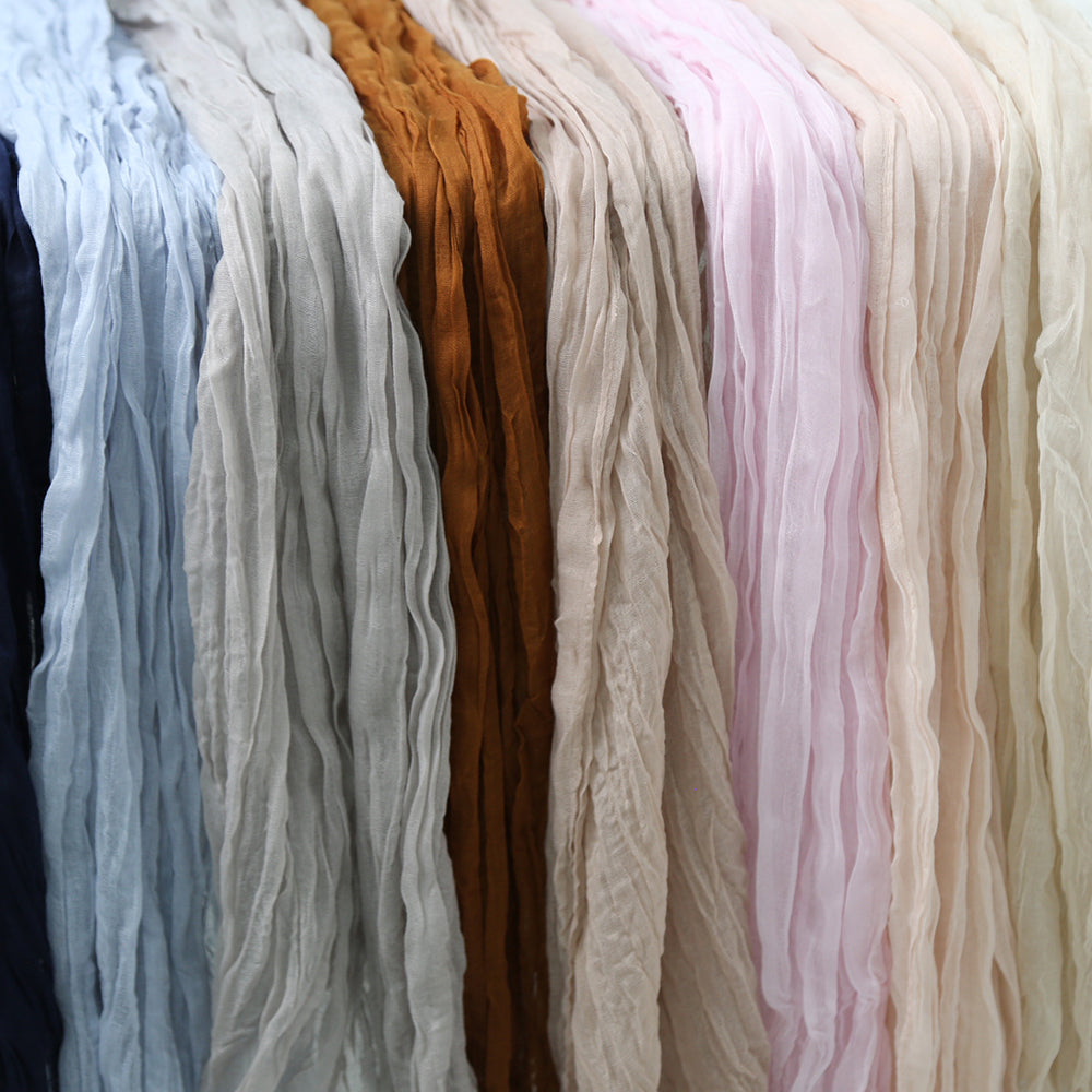 Gauze table runners available in various colors, featuring a soft, textured fabric. The range of colors includes burnt orange, blush pink, dusty blue, dusty pink, ivory cream, light grey, navy, off white, olive green, and sand. Each runner adds a unique and stylish touch to table settings, enhancing the overall ambiance with their elegant and versatile design.