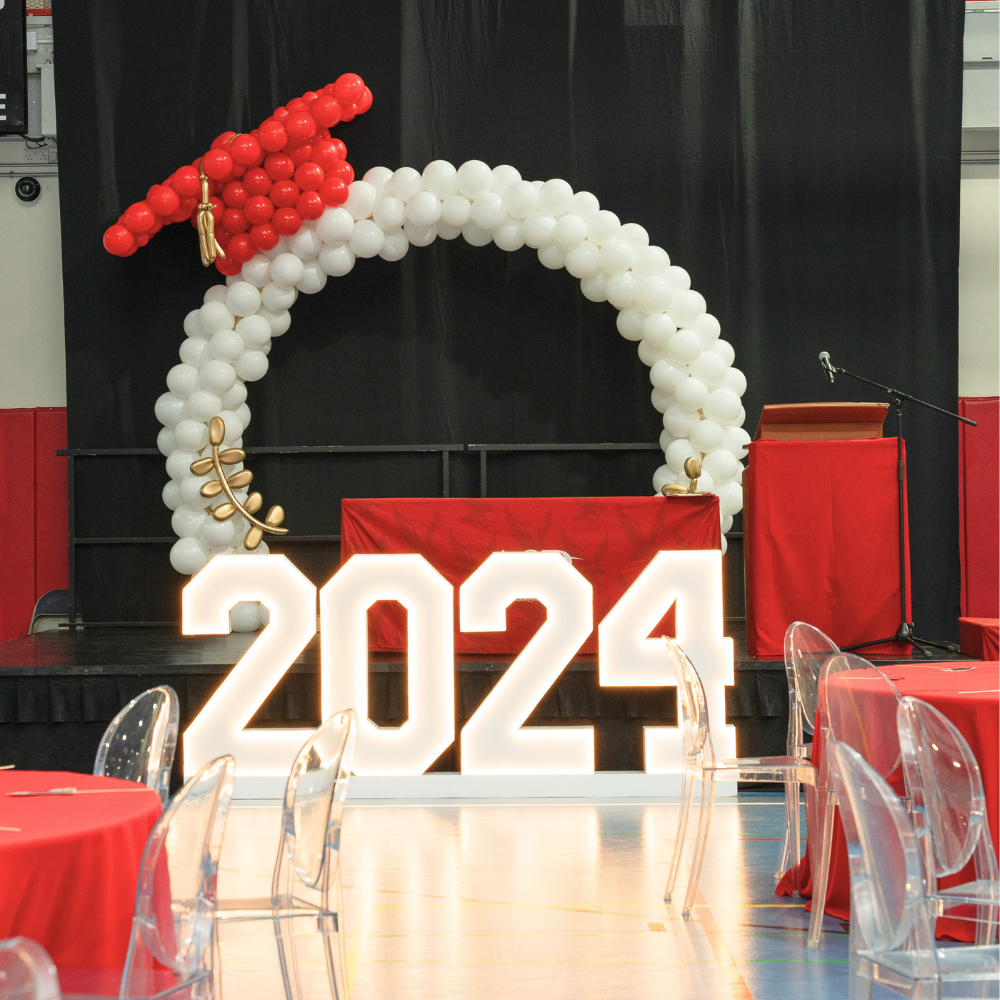 A graduation cap round balloon arch in white and red, featuring a celebratory and vibrant design. Made from durable plastic and metal, this arch adds a festive touch to graduation parties and ceremonies, creating a striking visual centerpiece.