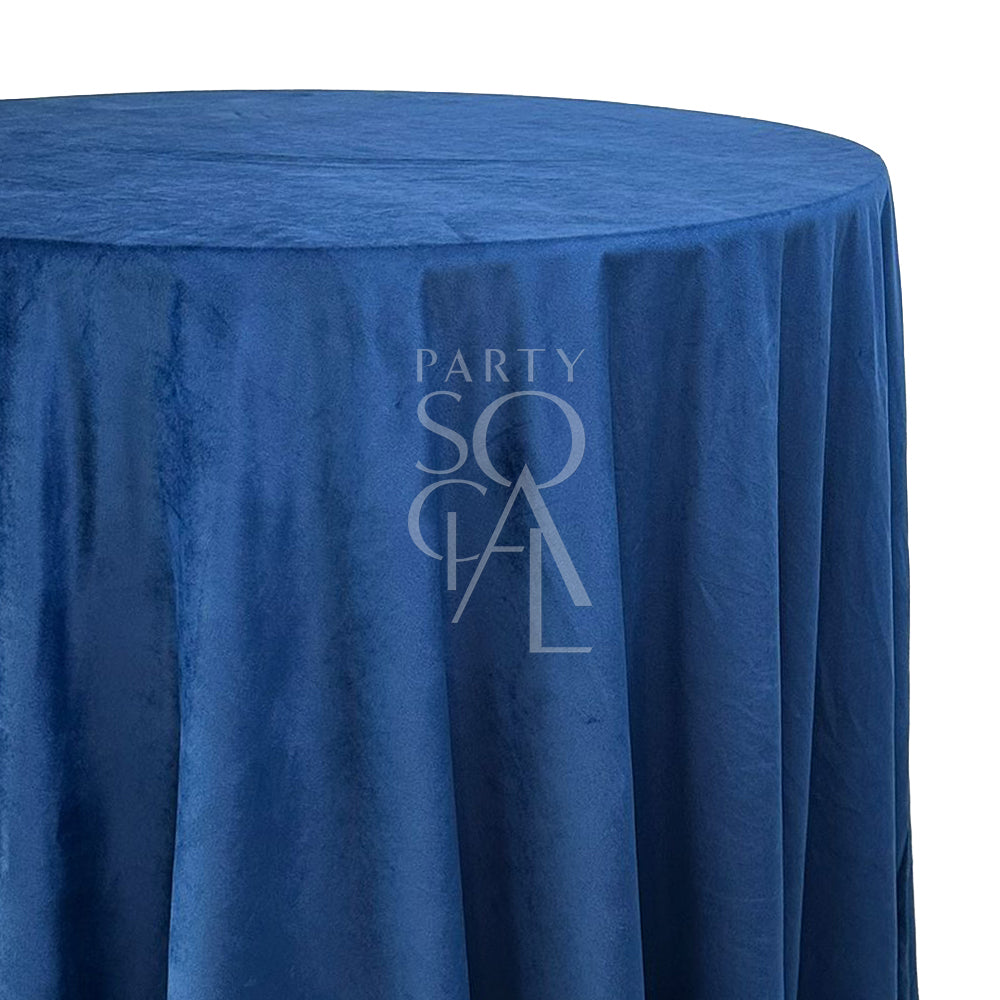 A round velvet tablecloth in deep blue, showcasing a rich and vibrant color. This luxurious tablecloth adds a dramatic and sophisticated touch to your dining setting, perfect for formal dinners and upscale events.