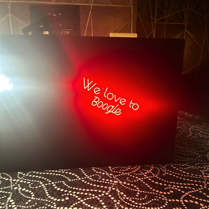 A &quot;We Love To Boogie&quot; LED neon sign in red, featuring a bold and vibrant design. This eye-catching sign is suitable for indoor use, adding a fun and energetic touch to parties, events, or home decor with its lively and nostalgic vibe.