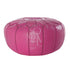 Moroccan leather pouf in bold fuchsia, with ornate embossed patterns and a circular shape.